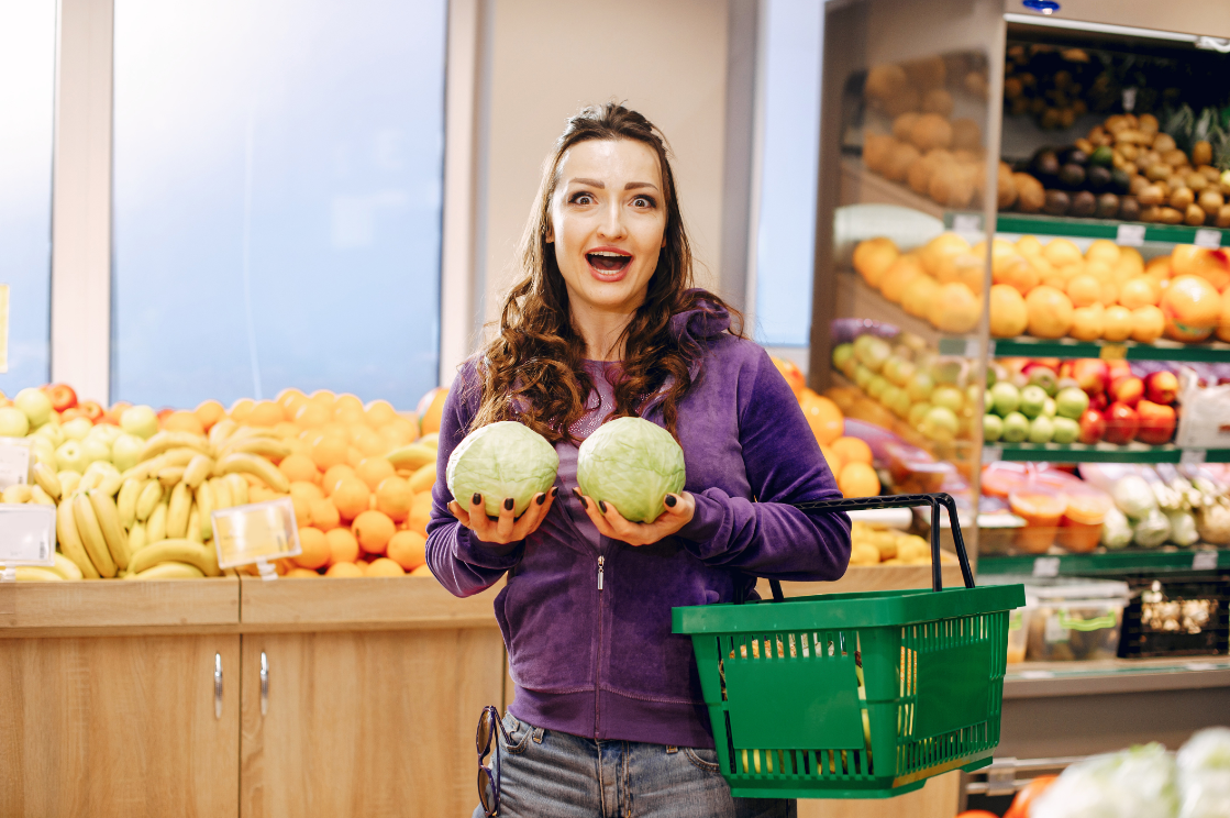 Девушка держит в руках капусту белокочанную на фоне продуктового магазина