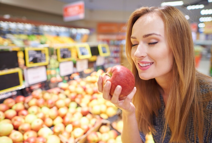 Девушка держит в руках яблоко на фоне продуктового магазина